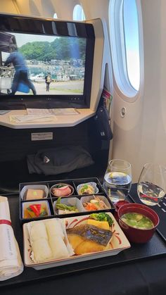 an airplane tray with food on it and a tv in the back ground behind it