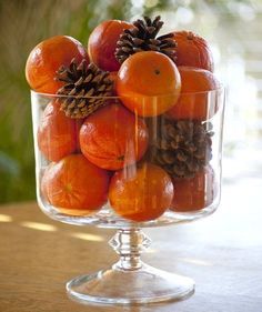 a glass bowl filled with oranges and pine cones