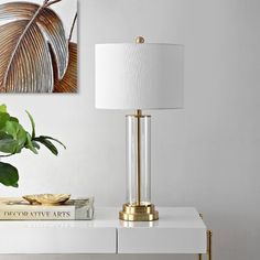 a white table with a gold lamp on it and a painting hanging above the table