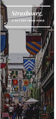 people walking down an alley way with flags hanging from the buildings and signs above them that read, strasburg a daytrip from paris