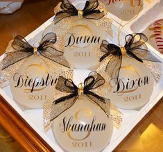 four personalized christmas ornament on a white tray with black and gold bows