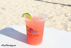 a drink sitting on top of a white table next to the ocean with a slice of lime