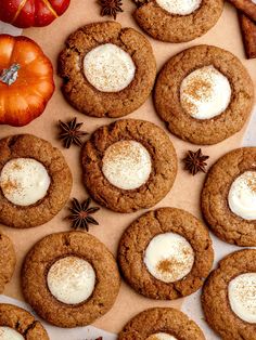 several cookies with white cream are arranged on a table next to pumpkins and spices