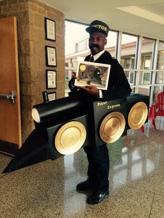 a man in a black suit and hat holding a cardboard car