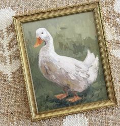 an oil painting of a white duck in a gold frame on a beige fabric background