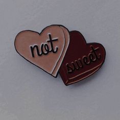 two heart shaped pins with the words not sweet written on them, sitting side by side