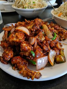 a white plate topped with meat and veggies next to bowls filled with rice