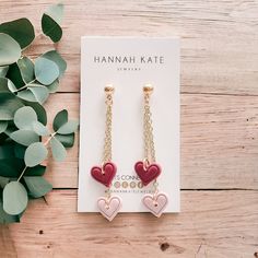 two heart shaped earrings sitting on top of a wooden table next to a green plant