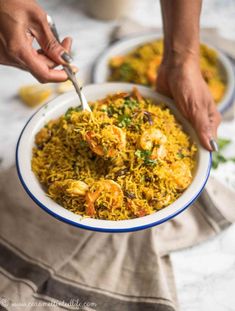 two hands are scooping rice out of a bowl with shrimp and vegetables in it