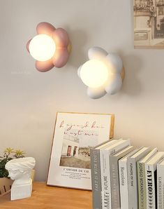 two lights that are on the side of a wall next to books and a plant