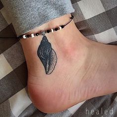 a woman's foot with a black and white shell tattoo on the side of her ankle