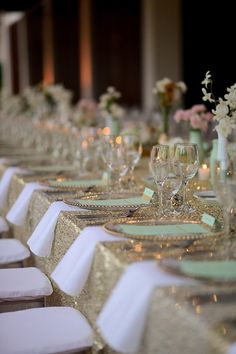 a long table is set with white and gold linens, green placemats, and wine glasses