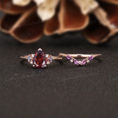 two engagement rings with pink and purple stones on them, sitting next to a flower