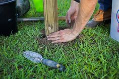 a person digging dirt in the ground next to a wooden pole and shovel with two hands on it