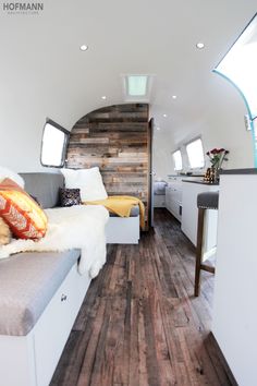 the interior of a camper with wood flooring and white walls, including a bed