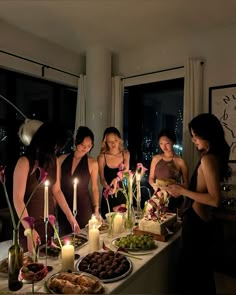 a group of women standing around a table with food and candles on top of it