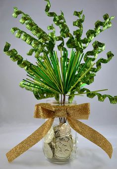 a vase filled with lots of green plants and gold ribbon on top of it's side