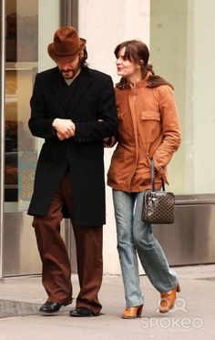 the man and woman are walking down the street looking at their cell phones while holding hands