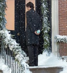 a woman is standing in the doorway of a building with snow on the ground and stairs