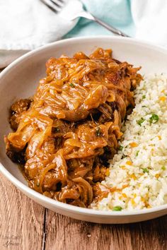 a white bowl filled with rice and meat next to a fork on a wooden table