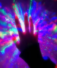 a person's hand in front of a multicolored background with light shining through it