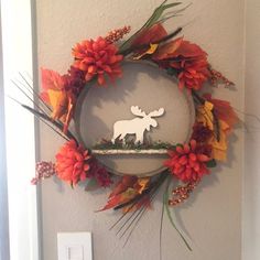 a wreath with a moose on it hanging from the wall next to a light switch