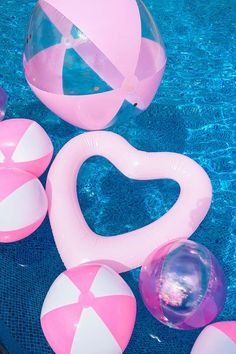 an inflatable heart shaped pool float next to several beach balls and floats on the edge of a swimming pool