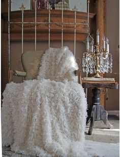 a chair covered in white fluffy material next to a chandelier