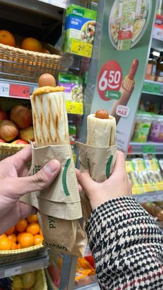 two people holding up some food in their hands at the grocery store with oranges and other produce behind them