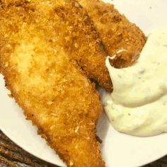 two fried fish fillets on a white plate with ranch dip and sour cream sauce