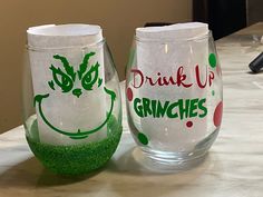 two wine glasses sitting on top of a table next to each other, with the words drink up gringies painted on them