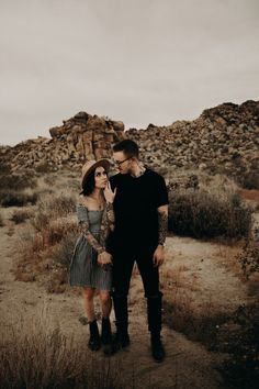 a man and woman standing next to each other on a dirt path in the desert