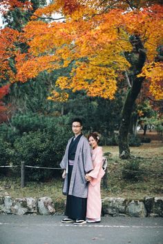 a man and woman dressed in traditional japanese garb standing next to each other on the street