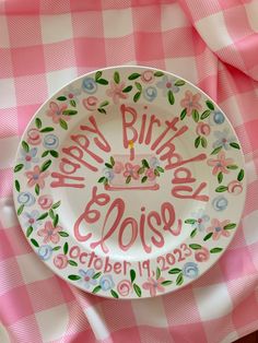 a pink and white plate with the words happy birthday rose on it sitting on a checkered table cloth