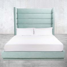 an upholstered bed with white sheets and pillows in a light blue color scheme