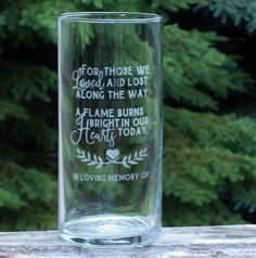 a clear glass with the words on it sitting on a wooden table in front of some trees