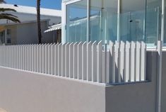 a white picket fence next to a house with palm trees in the backgroud