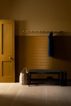 a bench and coat rack in a room with wooden floors, yellow doors and brown walls