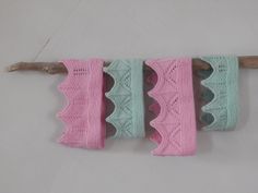 three knitted clothes hanging from a wooden stick on a white wall with pink and green trim