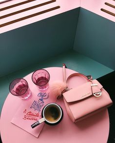 a pink table topped with a cup of coffee next to a handbag and two glasses