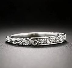 an antique style wedding ring with diamonds on the sides and in the middle, sitting on a black surface