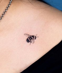 a small black and white bee tattoo on the back of a woman's shoulder