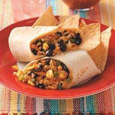 a burrito filled with beans and corn on a red plate next to tortilla chips