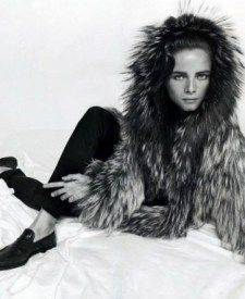 black and white photograph of woman in fur coat on bed