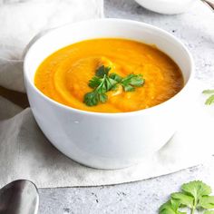 a white bowl filled with carrot soup and garnished with parsley