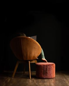 a person sitting in a chair reading a book on the floor next to a stool