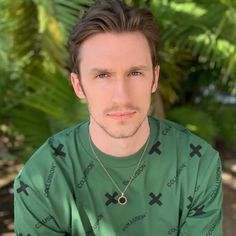 a man wearing a green t - shirt with crosses on it is looking at the camera