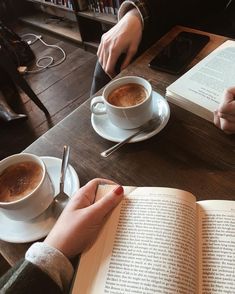 two people sitting at a table with coffee and an open book