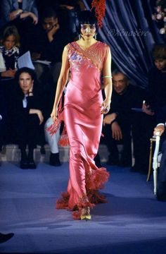 a woman walking down a runway in a pink dress with feathers on it's head