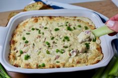 a person dipping something into a casserole with green onions and celery